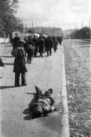 Babi-Yar Corpses on the sidewalk. Young boy stops to look at a murdered corpse.  Location is  the right side of Pobeda Avenue